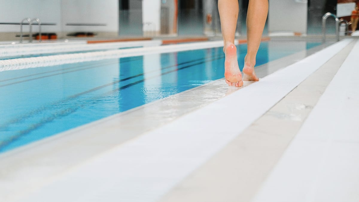 Pieds nus sur la margelle mouillée d'une piscine couverte